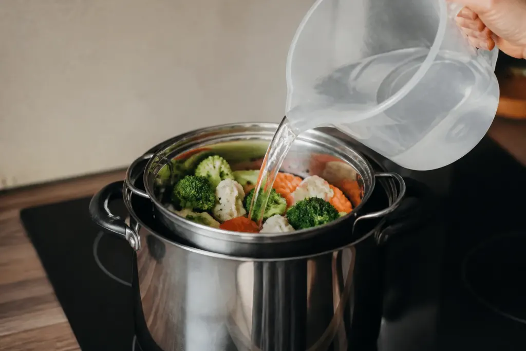 Eau versée dans cocotte vapeur avec panier legumes