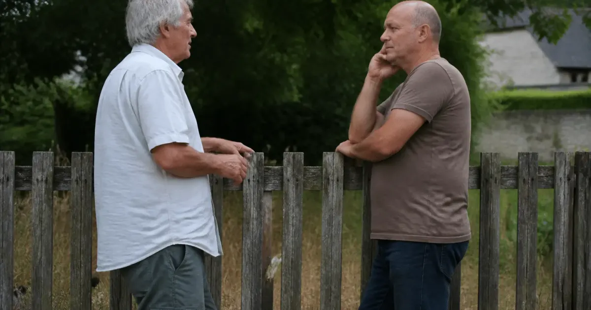 Deux hommes debout devant une clôture en bois usée discutant