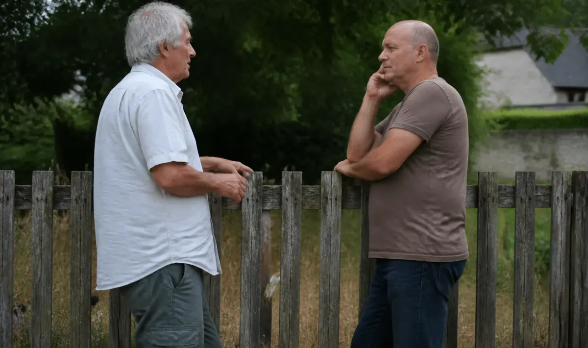 Deux hommes debout devant une clôture en bois usée discutant