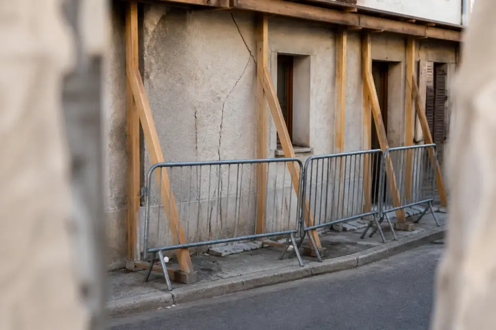 Barrieres grises et etais en bois devant facade fissuree