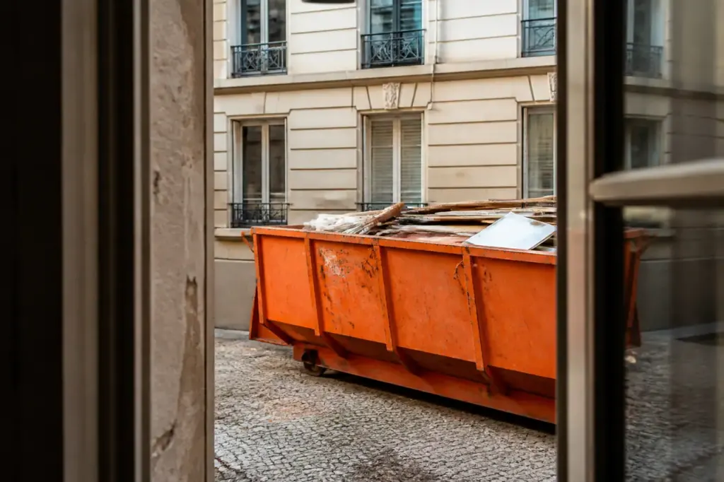 Benne de chantier orange stationnant devant un immeuble