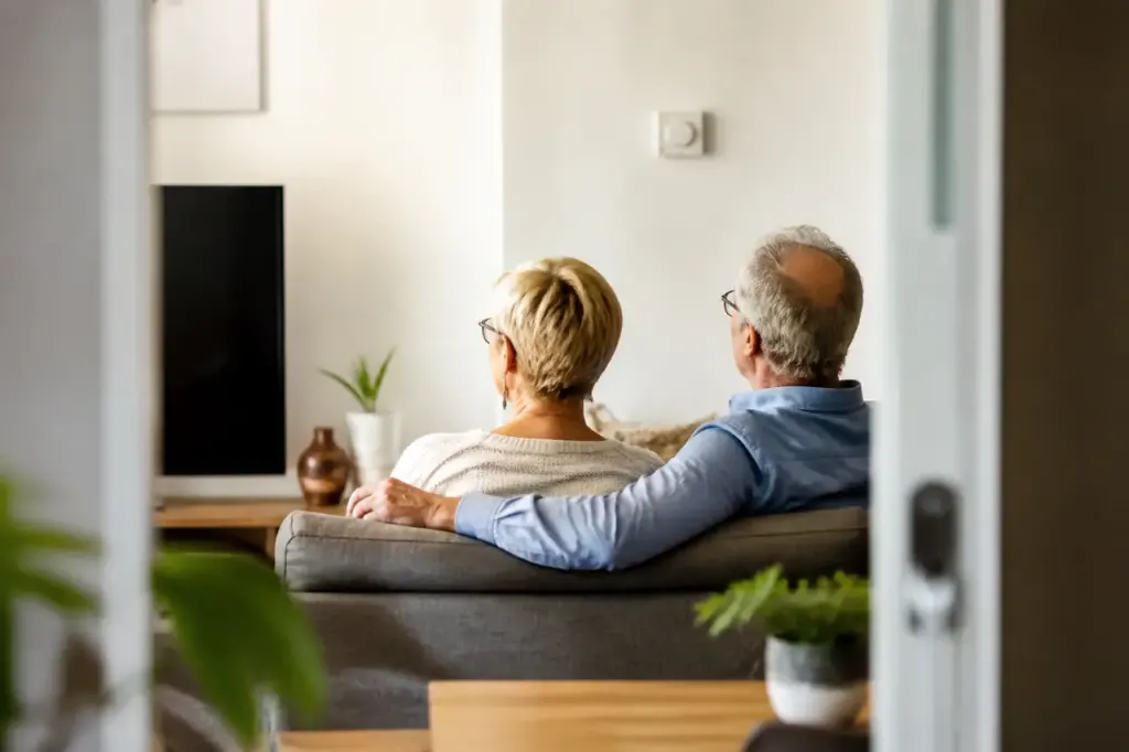 Couple âgé assis dans salon lumineux devant thermostat blanc