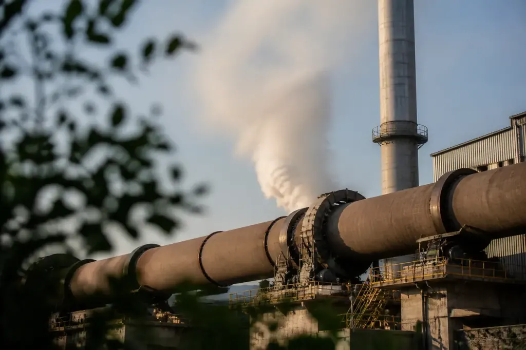 Four rotatif de cimenterie fumant devant une cheminee metallique