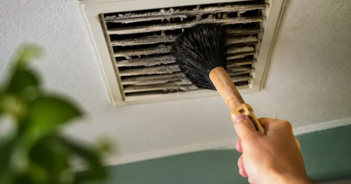 Grille de VMC poussiereuse au plafond, brosse en main