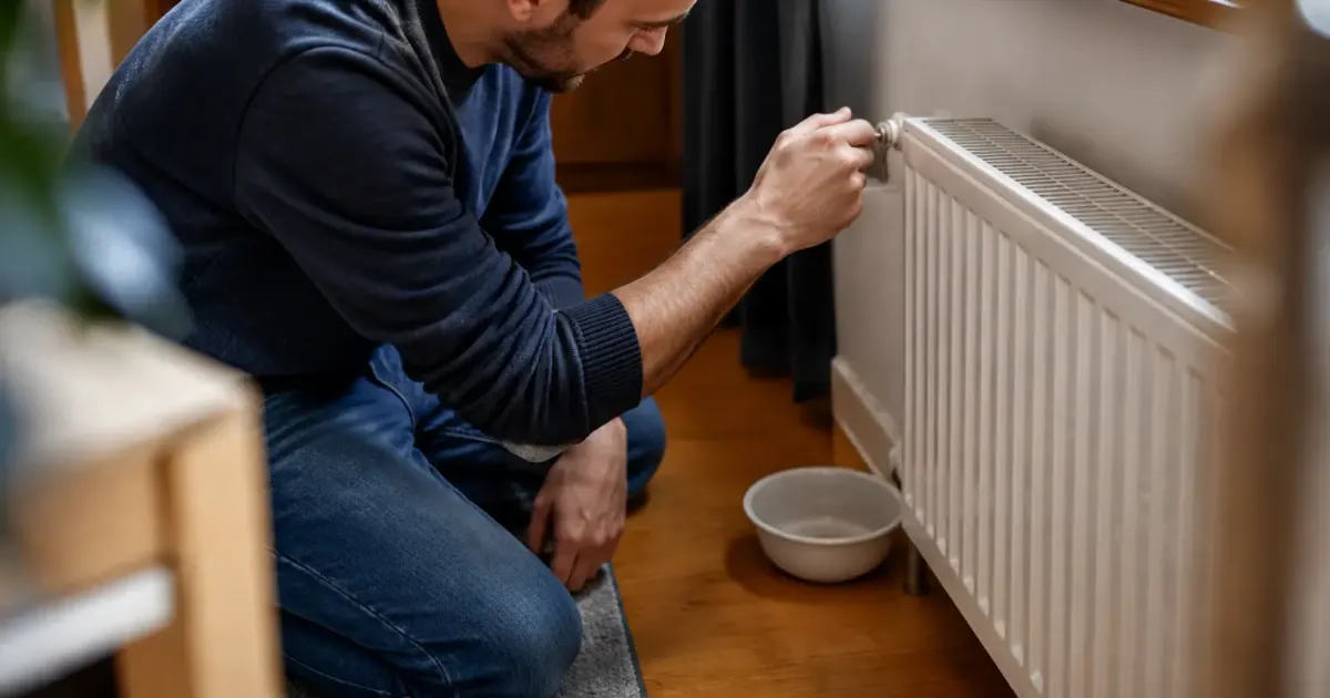 Homme agenouille purgeant un radiateur avec une petite cle