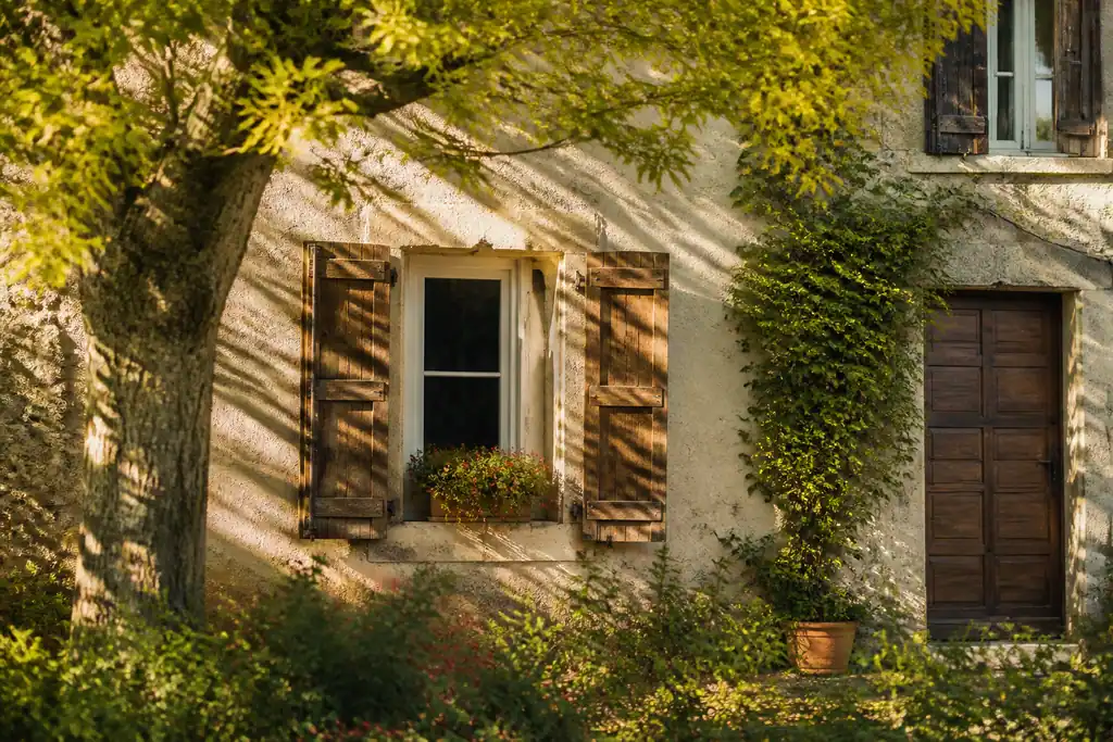 Maison avec volets en bois et arbre au soleil