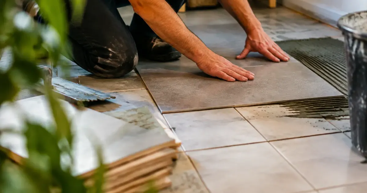 Ouvrier accroupi collant des plaques sur carrelage existant